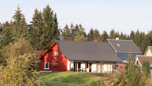 A red house with a sloped roof, surrounded by trees and a grassy yard. - Enjoy the Thuringian Forest in the barrier-free vacation home "Bergwiese" (Neuhaus am Rennweg)