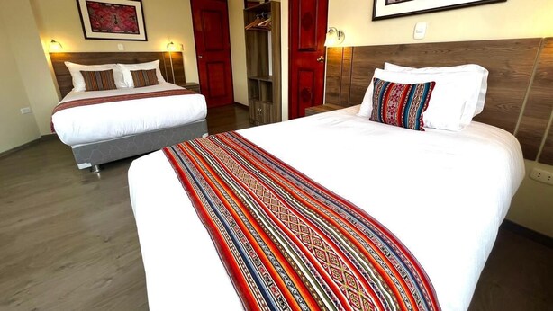 Een hotelkamer met twee bedden, een houten vloer en een rode deur.