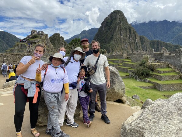 Un grupo de personas en Machu Picchu, frente a antiguas estructuras de piedra, con una montaña al fondo.