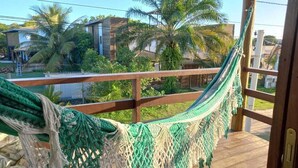 A hammock on a wooden deck with a view of palm trees and houses. - Pousada Cantinho de taipu (Maraú)
