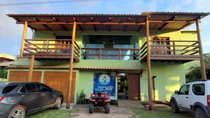 A two-story building with a balcony, a signboard, and two cars parked in front. - Pousada Cantinho de taipu (Maraú)