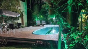 A pool area with lounge chairs and umbrellas, surrounded by lush greenery and palm trees. - Pousada Cantinho de taipu (Maraú)