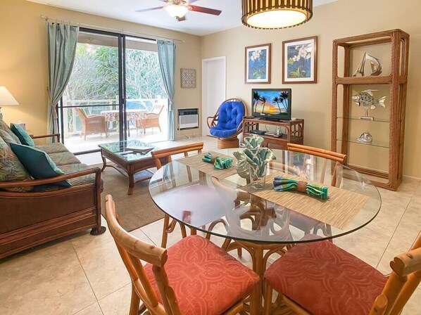 A spacious living room with a glass dining table, comfortable seating, a television, and a decorative fish tank.
