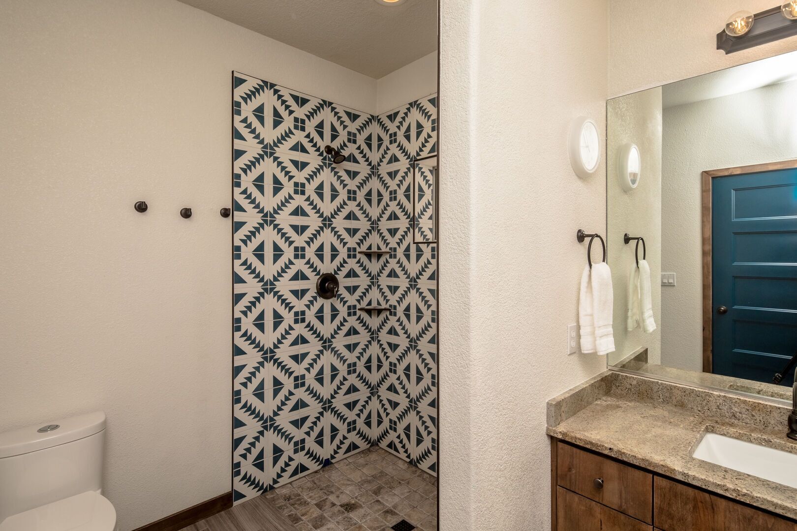 A bathroom with a patterned shower door, a white toilet, a sink with a granite countertop, and a mirror above the sink.