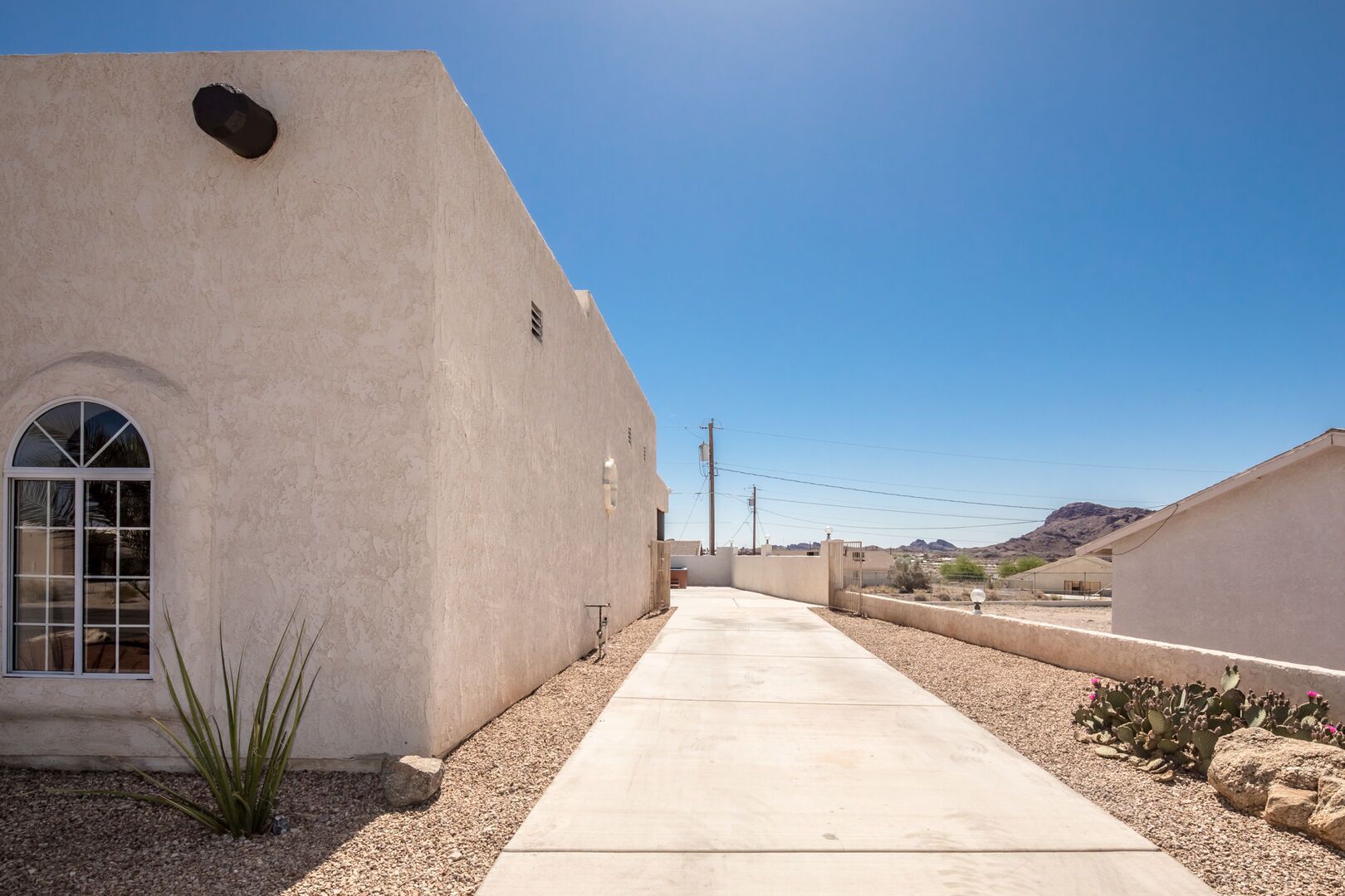 A building with a large arched window and a flat roof, surrounded by a gravel path and sparse vegetation.
