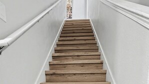 A wooden staircase with white walls and a tiled floor.