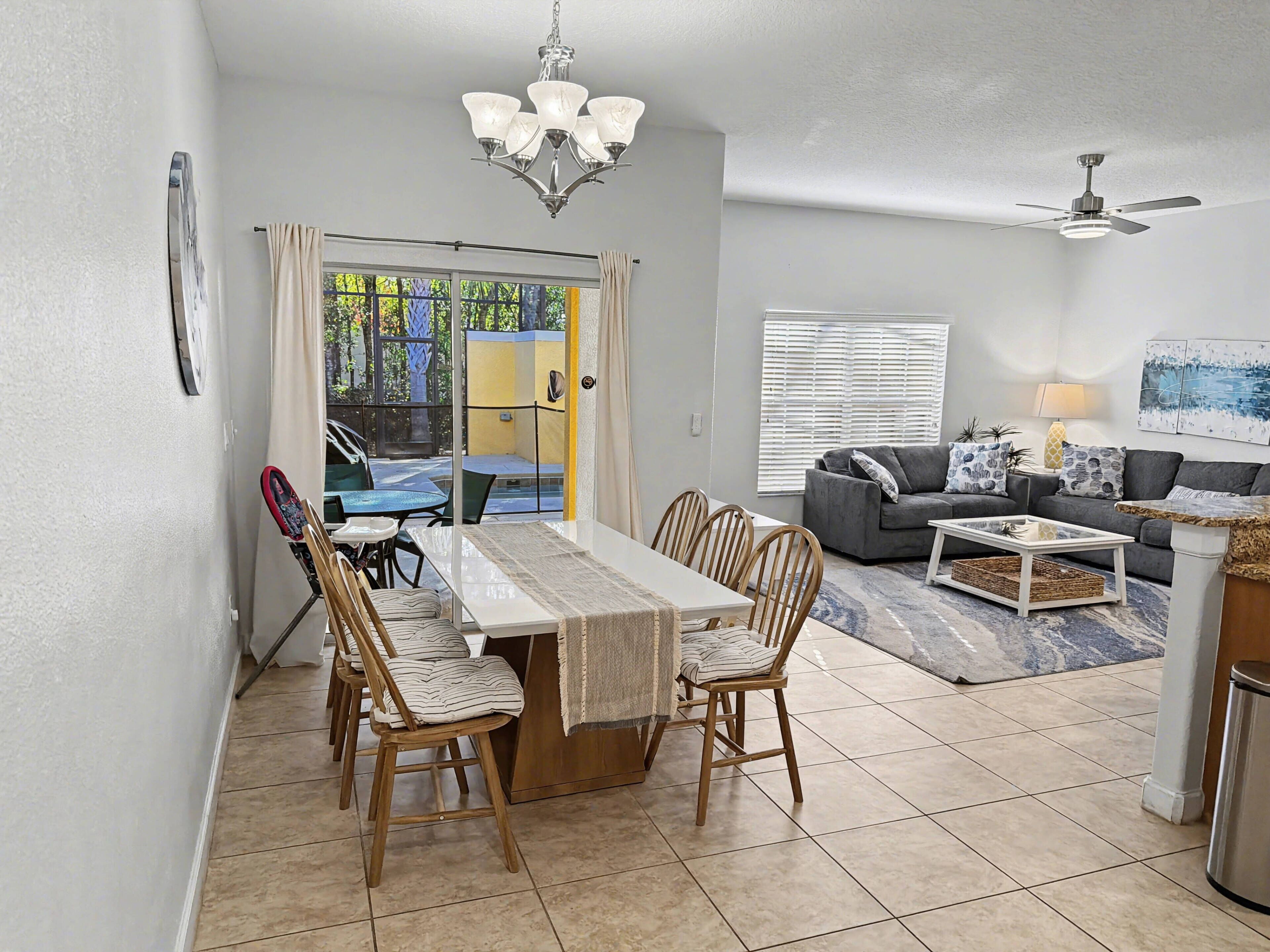 A dining area with a table and chairs, a sofa, a ceiling fan, and a window with blinds.