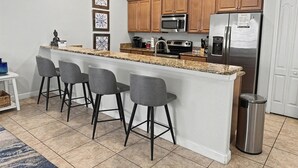 A modern kitchen with a granite countertop, stainless steel appliances, wooden cabinets, and bar stools.