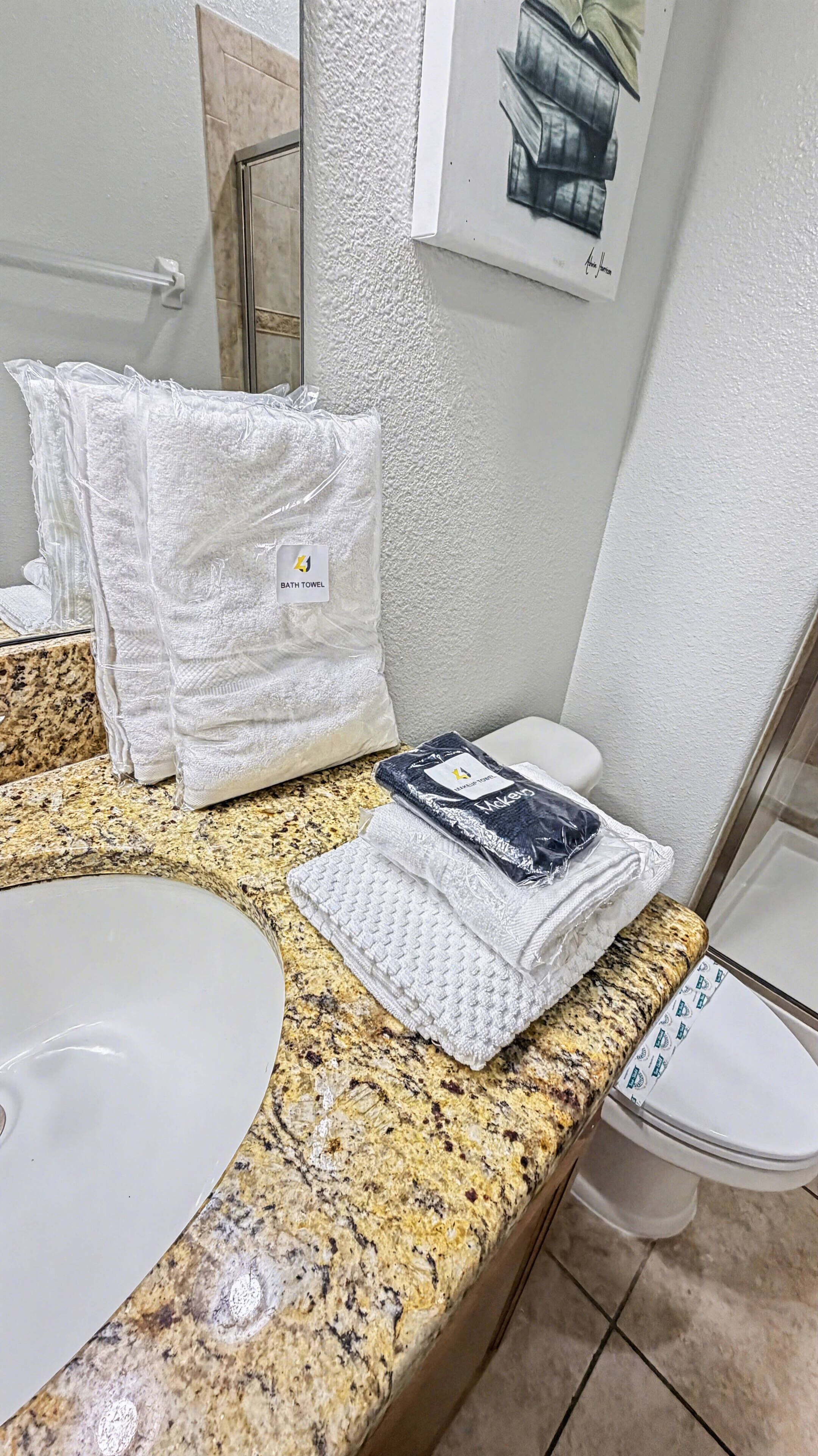 A bathroom with a granite countertop, a white sink, a toilet, and a towel rack with folded towels.