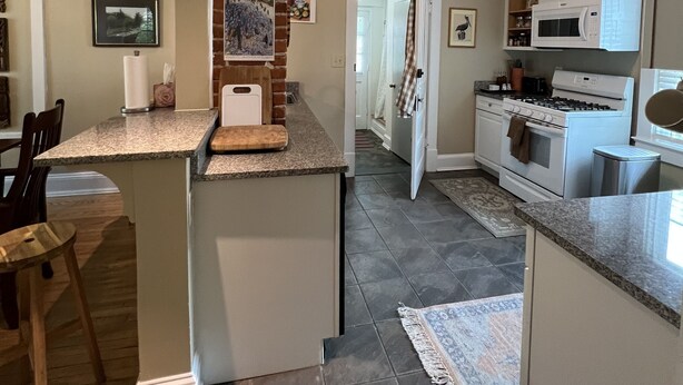 A kitchen with a central island, a brick accent wall, a microwave, stove, and a sink. - Stadium Hill House (Charlottesville)