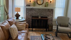 A living room with a brick fireplace, leather sofa, and a ceiling fan. - Stadium Hill House (Charlottesville)