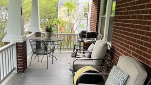 A covered porch with a ceiling fan, a table with chairs, and a sofa with cushions. - Stadium Hill House (Charlottesville)