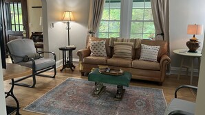 A living room with a brown sofa, a green ottoman, and a patterned rug. - Stadium Hill House (Charlottesville)
