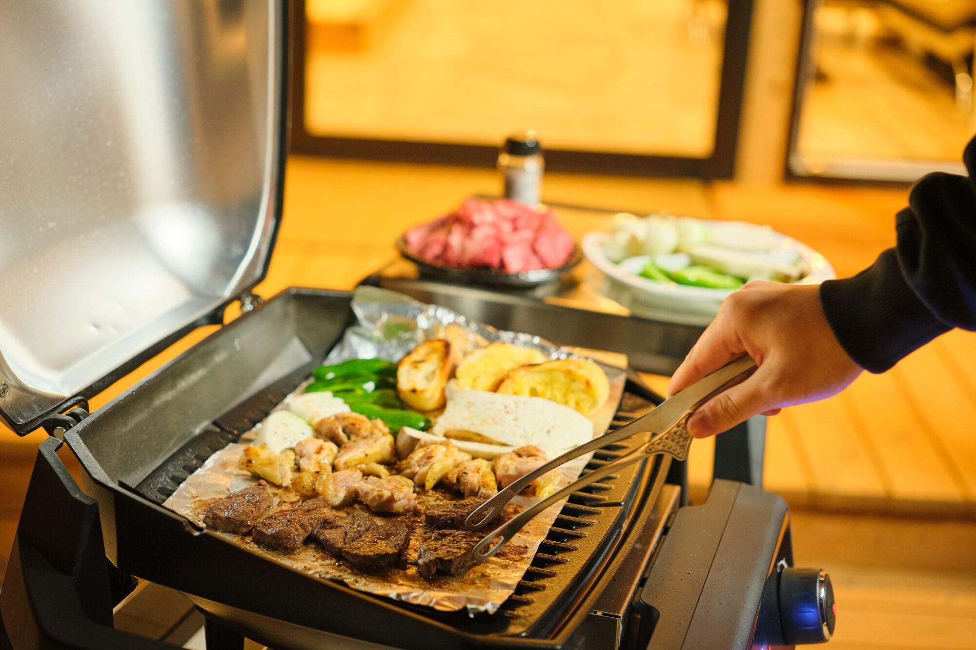 A person grilling various meats and vegetables on an outdoor grill.