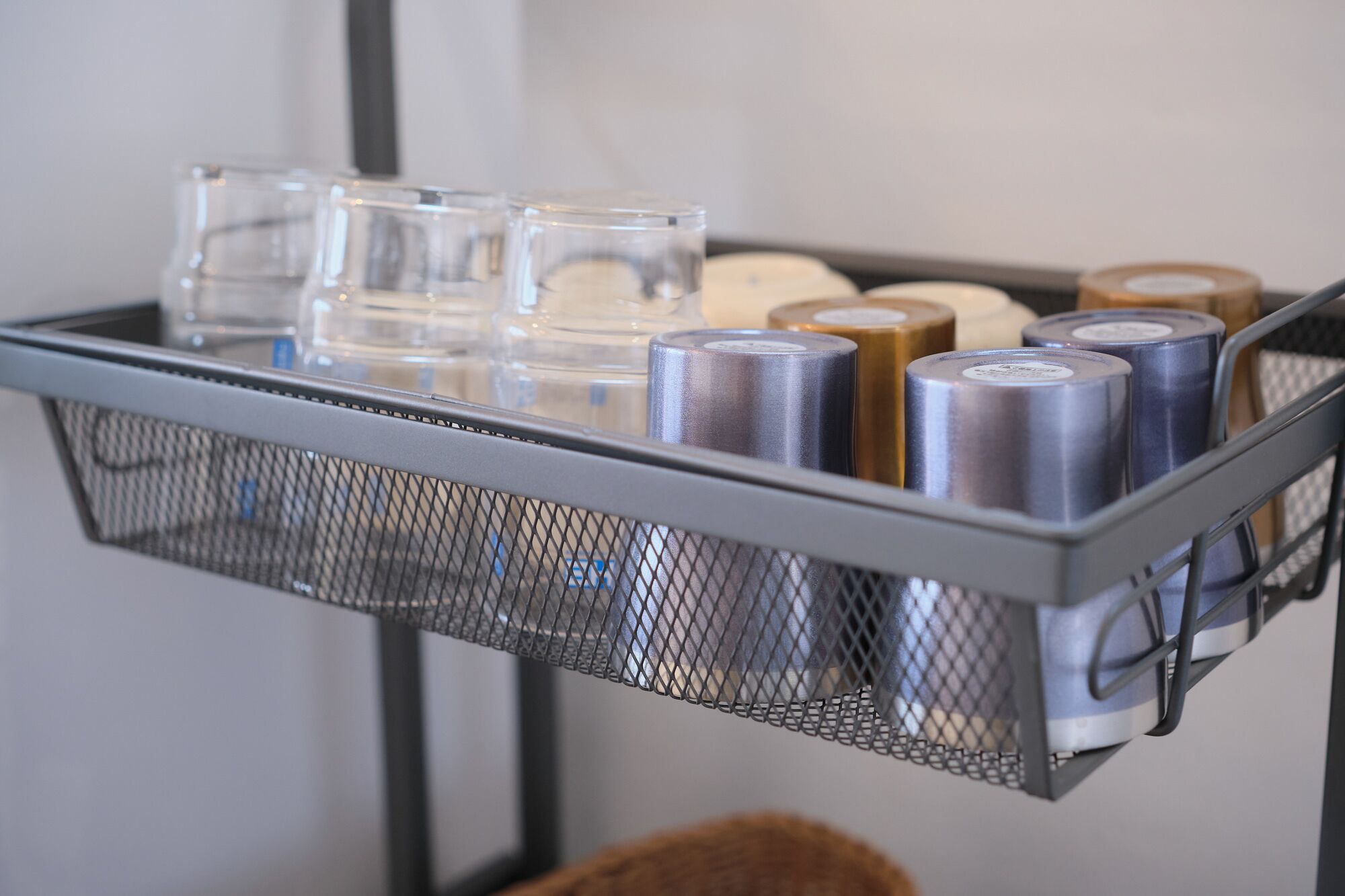 A metal cart with a mesh top holding various items including clear glasses, metal cans, and a brown bag.