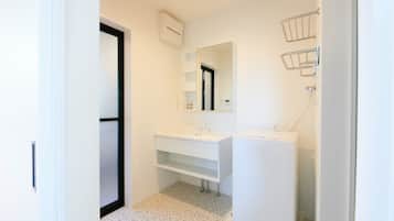 Une petite salle de bain propre, avec des éléments d’aménagement blancs, un miroir et un espace douche.