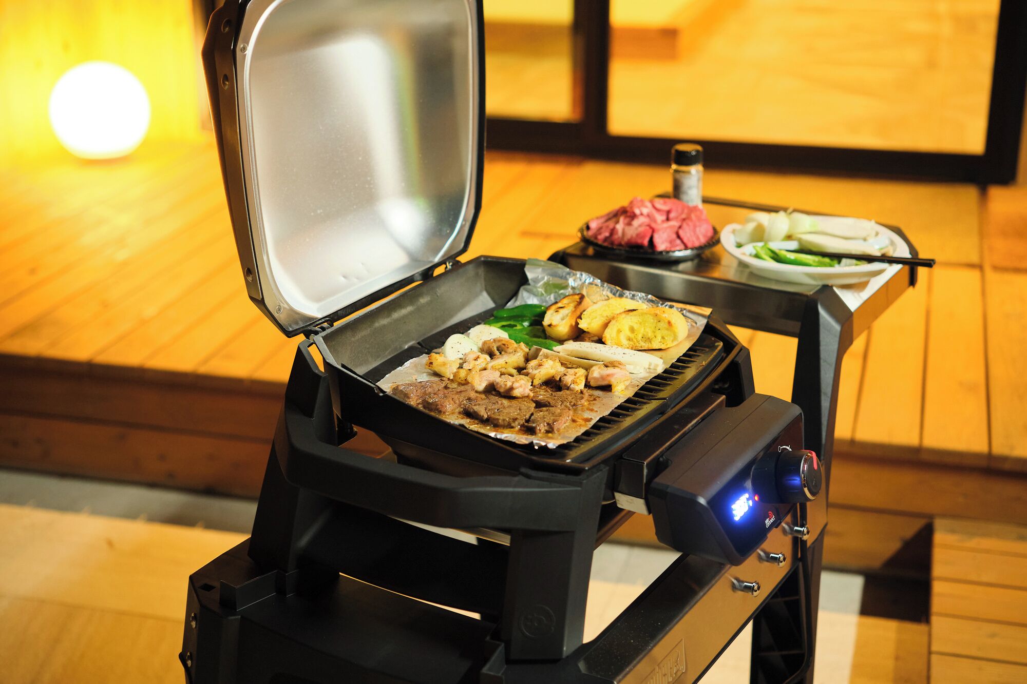 A portable grill with food on it, a bottle of sauce, and a plate with vegetables.