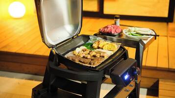 A portable grill with food on it, a bottle of sauce, and a plate with vegetables.