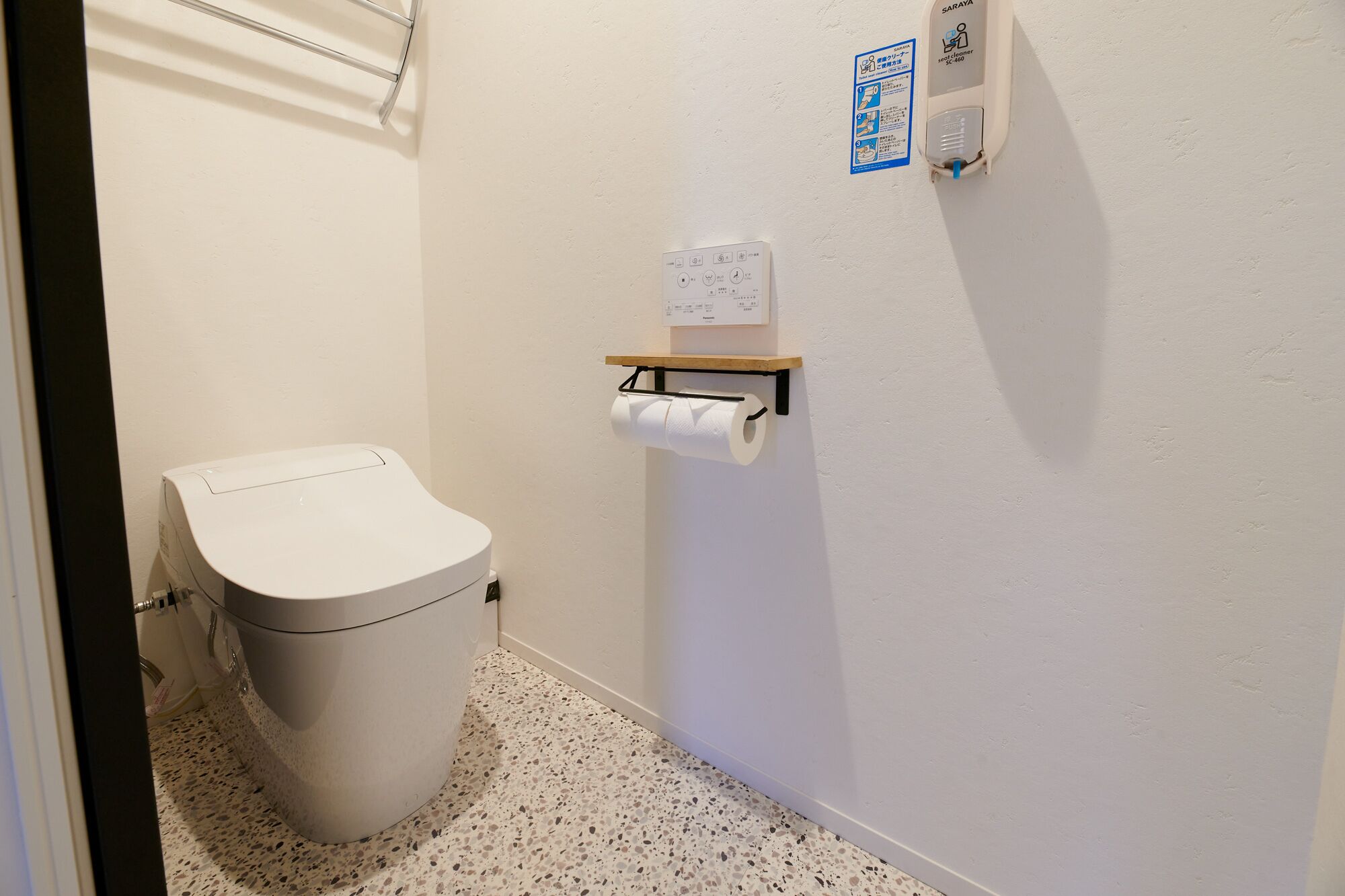 A small, compact bathroom with a toilet, a paper towel holder, and a hand dryer.