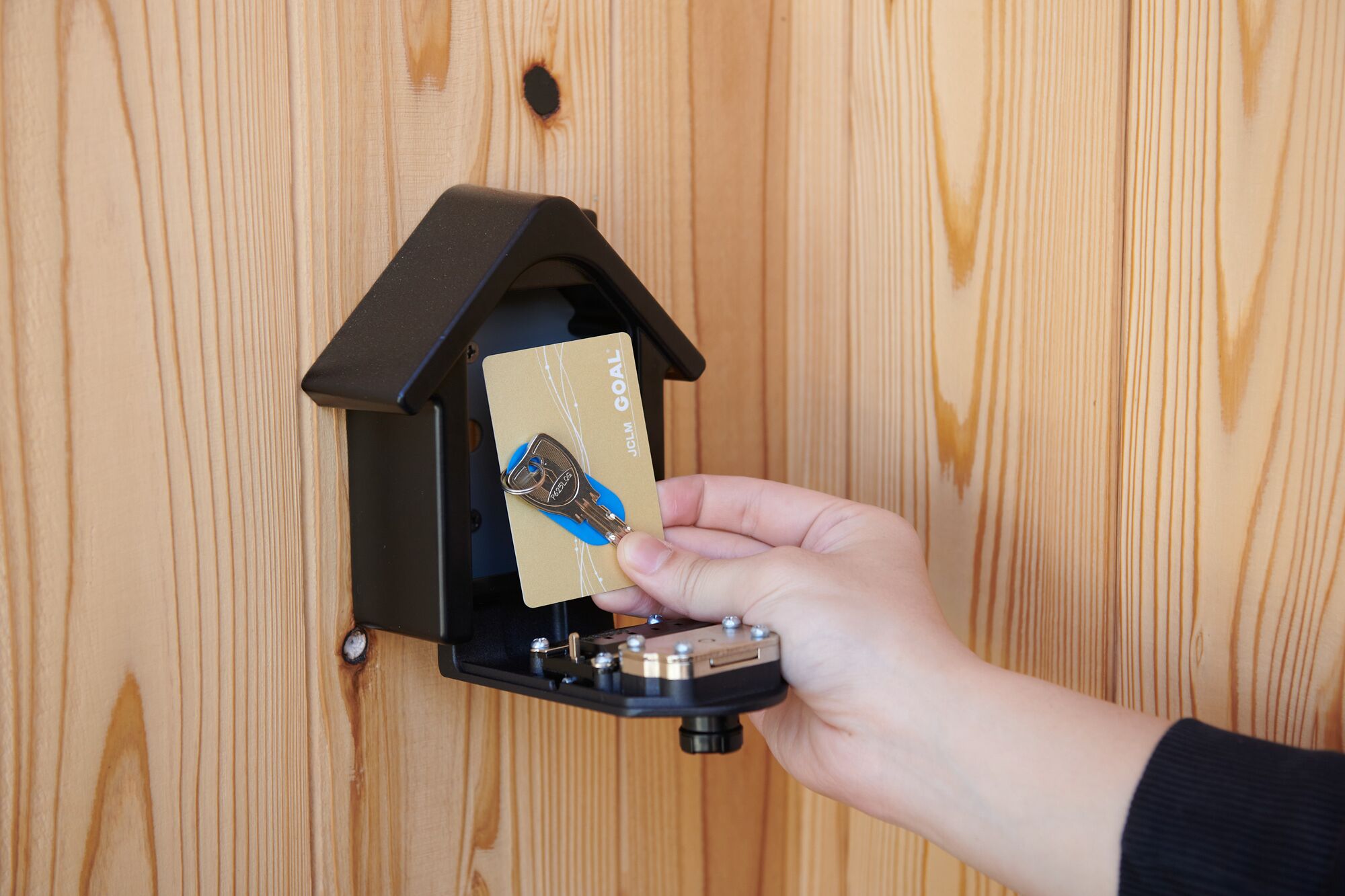 A hand inserting a key into a wooden door lock.