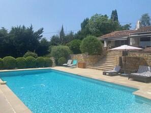 A swimming pool with clear blue water, surrounded by stone steps and lounge chairs.