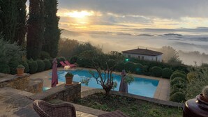 Un área de piscina con vistas al amanecer, rodeada de árboles y un pequeño edificio.