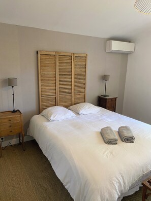 A neatly made bed with white linens, two bedside lamps, and a wooden headboard.