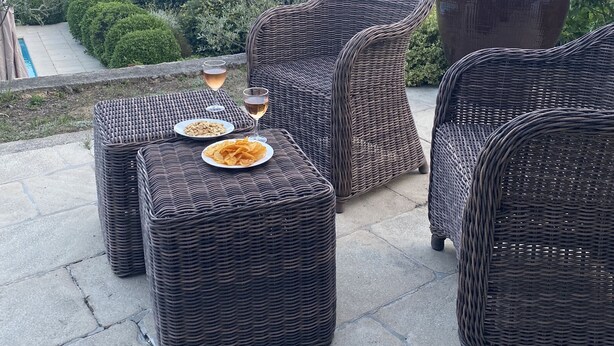 Mobiliario de mimbre con bandejas de bocadillos y bebidas, en un patio con vistas a un valle y colinas.