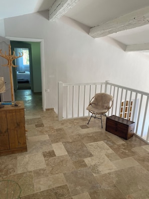 Ein Zimmer mit einer Holzkommode, einem Sessel und einer Treppe mit weißer Geländer.