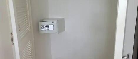 A small, white electrical box mounted on a wall in a corner of a room with a door and a vent.