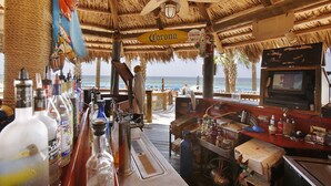 Un bar de playa con techo de paja, un letrero de Corona y vista al océano.