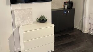 Una cucina moderna con una TV a schermo piatto montata sopra un armadietto bianco, un pavimento in legno scuro e una piccola pianta sull'armadietto.