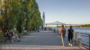 Una passeggiata lungo il fiume con panchine, una torre dell'orologio e un ponte sullo sfondo.