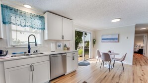 Een moderne keuken met witte kasten, een spoelbak en een vaatwasser. Er is een eethoek met een tafel en stoelen.