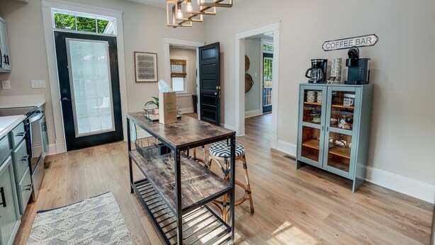 A modern kitchen with a wooden table, a coffee bar, and a hanging light fixture. - Hawthorn House Remodeled 3BR Walk to Town! (Colonial Beach)