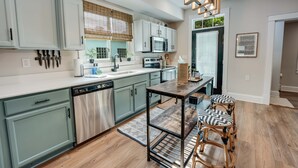 A modern kitchen with light green cabinets, stainless steel appliances, and a wooden dining table with two chairs. - Hawthorn House Remodeled 3BR Walk to Town! (Colonial Beach)