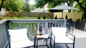 A deck with two white cushioned chairs and a small table, a bottle, and two wine glasses. - Hawthorn House Remodeled 3BR Walk to Town! (Colonial Beach)