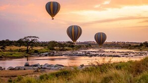 Three hot air balloons flying over a river with a savannah landscape in the background. - KUOOM SERENGETI (Serengeti)