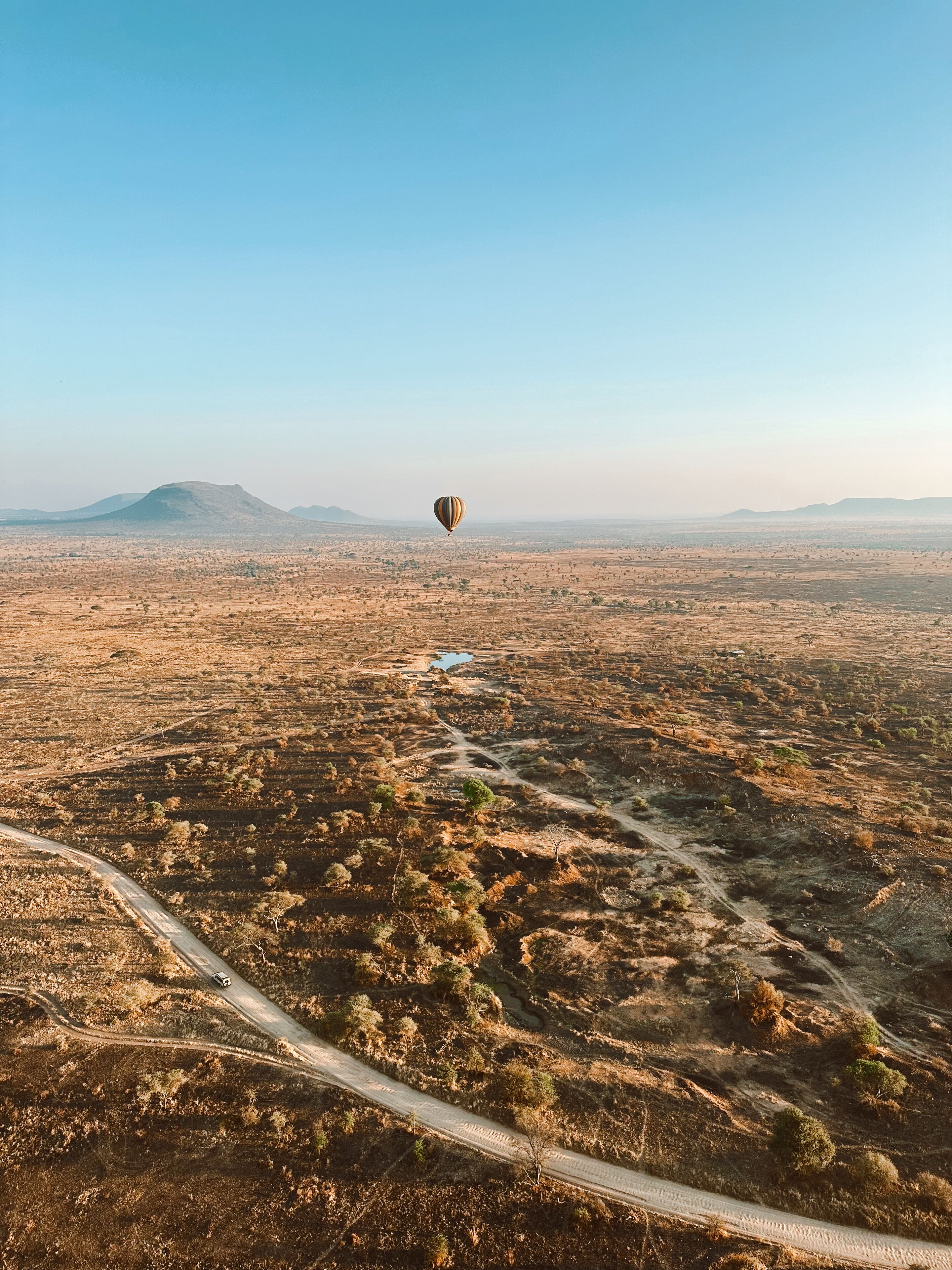 Un globo aerostático sobre un paisaje árido y montañoso, con vegetación escasa y un camino sinuoso.