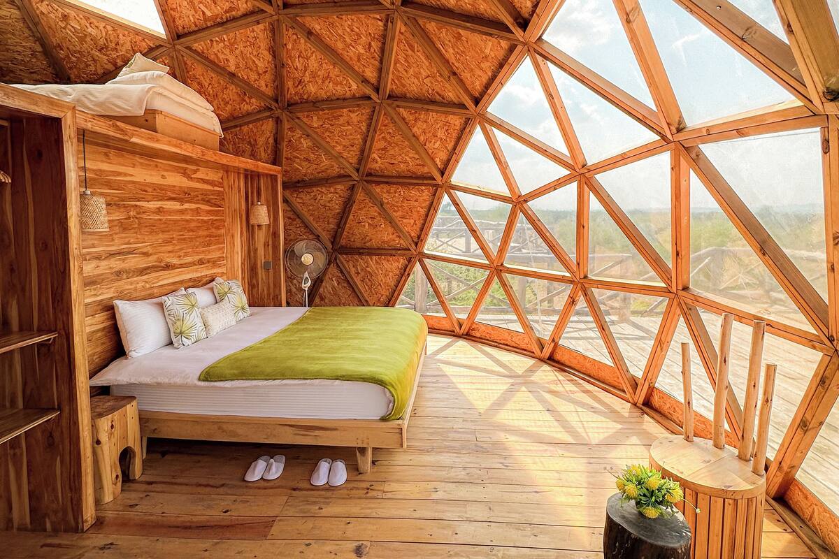 A wooden bedroom with a bed, a small stool, and a nightstand.