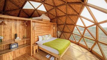 Een houten kamer met een hoge plafond, een bed met een groene deken, een houten dressoir en een klein krukje.