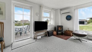 Quarto com televisão, lareira e grandes janelas com vista para um jardim.