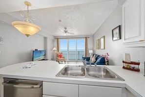 Une cuisine moderne dotée d’un grand îlot central, d’un ventilateur de plafond et offrant une vue sur l’océan grâce à de grandes portes-fenêtres coulissantes.