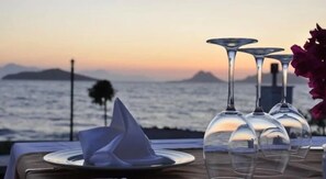 A table set with wine glasses and a folded napkin, overlooking a coastal view with a sunset. - Small Beach Hotel  (Bodrum)