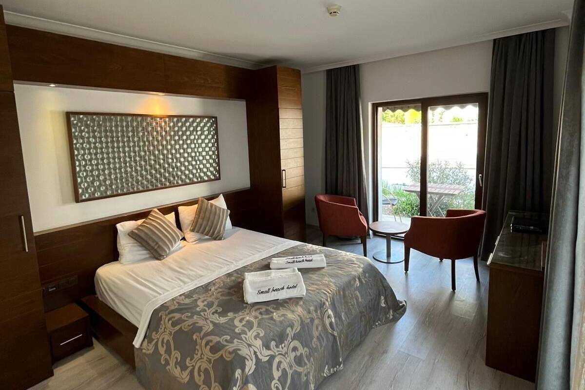 A modern hotel room with a large bed, a small desk, and a seating area with two chairs.