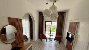 Une chambre d’hôtel moderne avec un plancher en bois, un miroir rond, un banc en bois, une table à manger avec des chaises et un téléviseur fixé au mur.