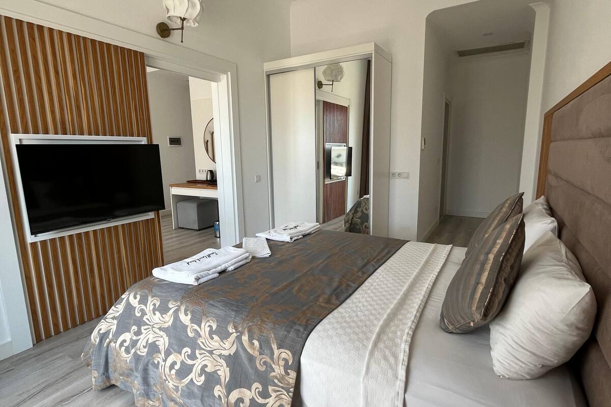 A modern hotel room with a large bed, a flat-screen TV mounted on the wall, and a wooden panel design on the wall.