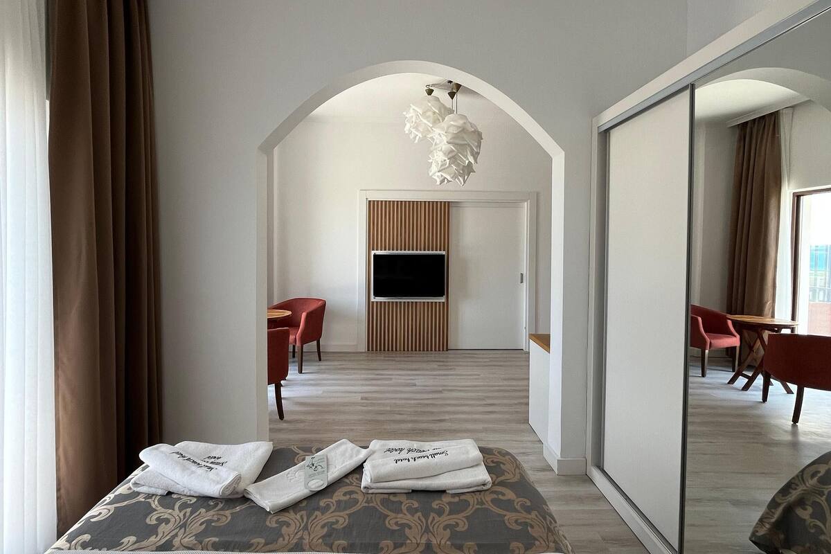 A modern hotel room with a large bed, a TV mounted on the wall, and a dining area with chairs.