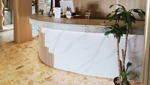 A reception desk with a curved design, a potted plant, and a tiled floor. - Hotel Toledo FL (Cartagena)