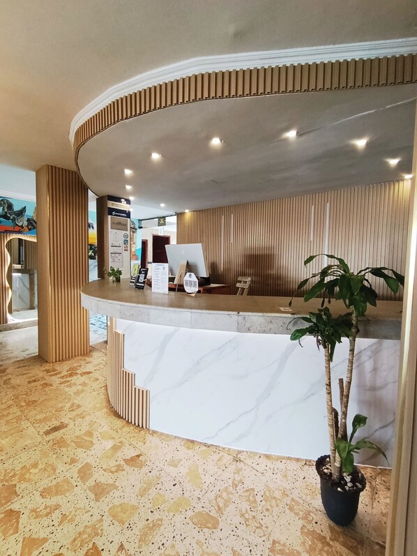 A reception desk with a curved design, a potted plant, and a tiled floor. - Hotel Toledo FL (Cartagena)